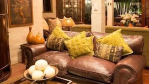 A cozy living room with a brown leather sofa, a wooden coffee table with decorative items, and a rustic ceiling with exposed beams.