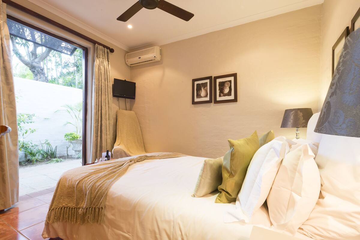 Un dormitorio con una cama, almohadas, un televisor y un equipo de aire acondicionado.