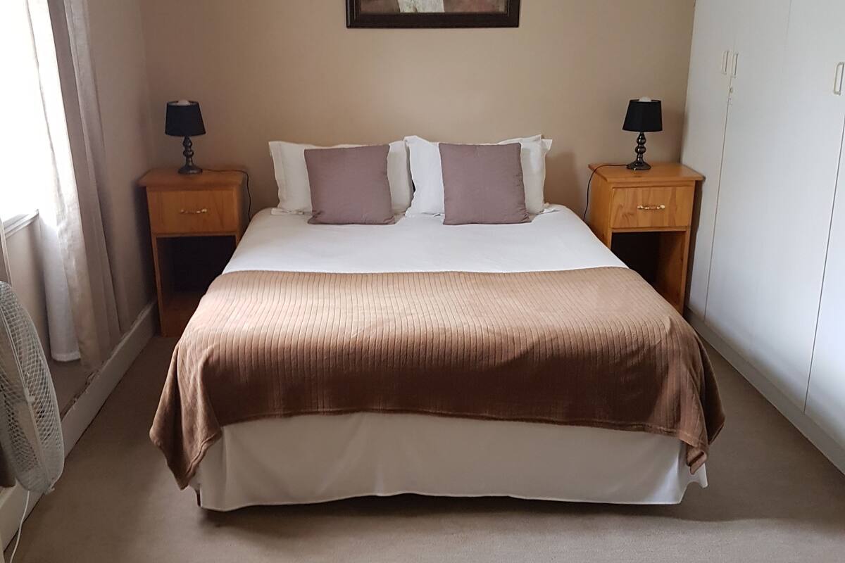 A bedroom with a large bed, two nightstands, a painting on the wall, and a wardrobe.