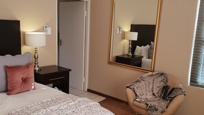 Un dormitorio con cama, mesita de noche, lámpara, silla, espejo y puerta.