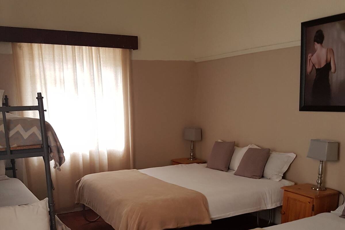 A hotel room with three beds, a wooden floor, a window with curtains, and a painting on the wall.