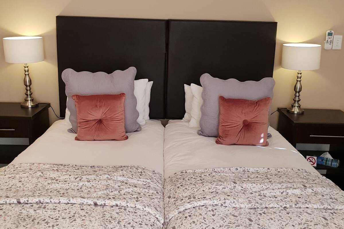 A double bed with a black headboard, two nightstands with lamps, and a patterned bedspread.