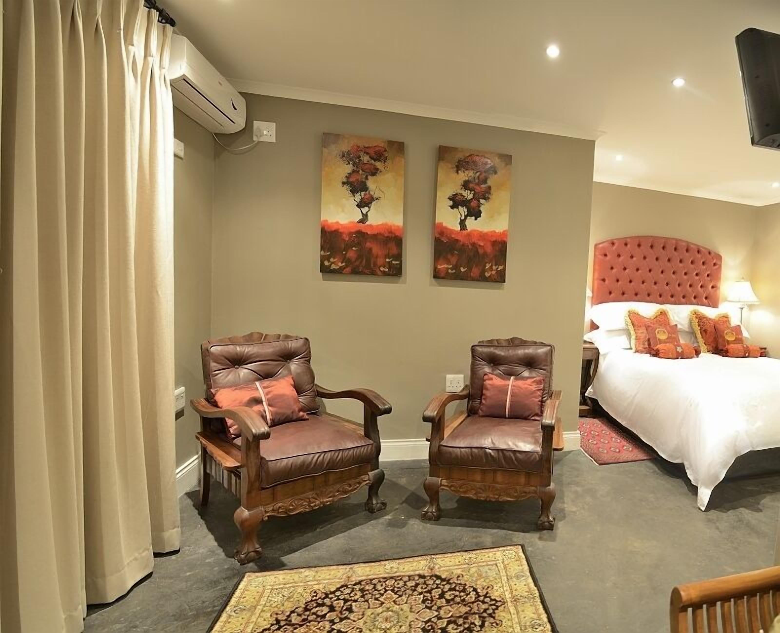 A hotel room with a bed, two armchairs, a rug, and two paintings on the wall.