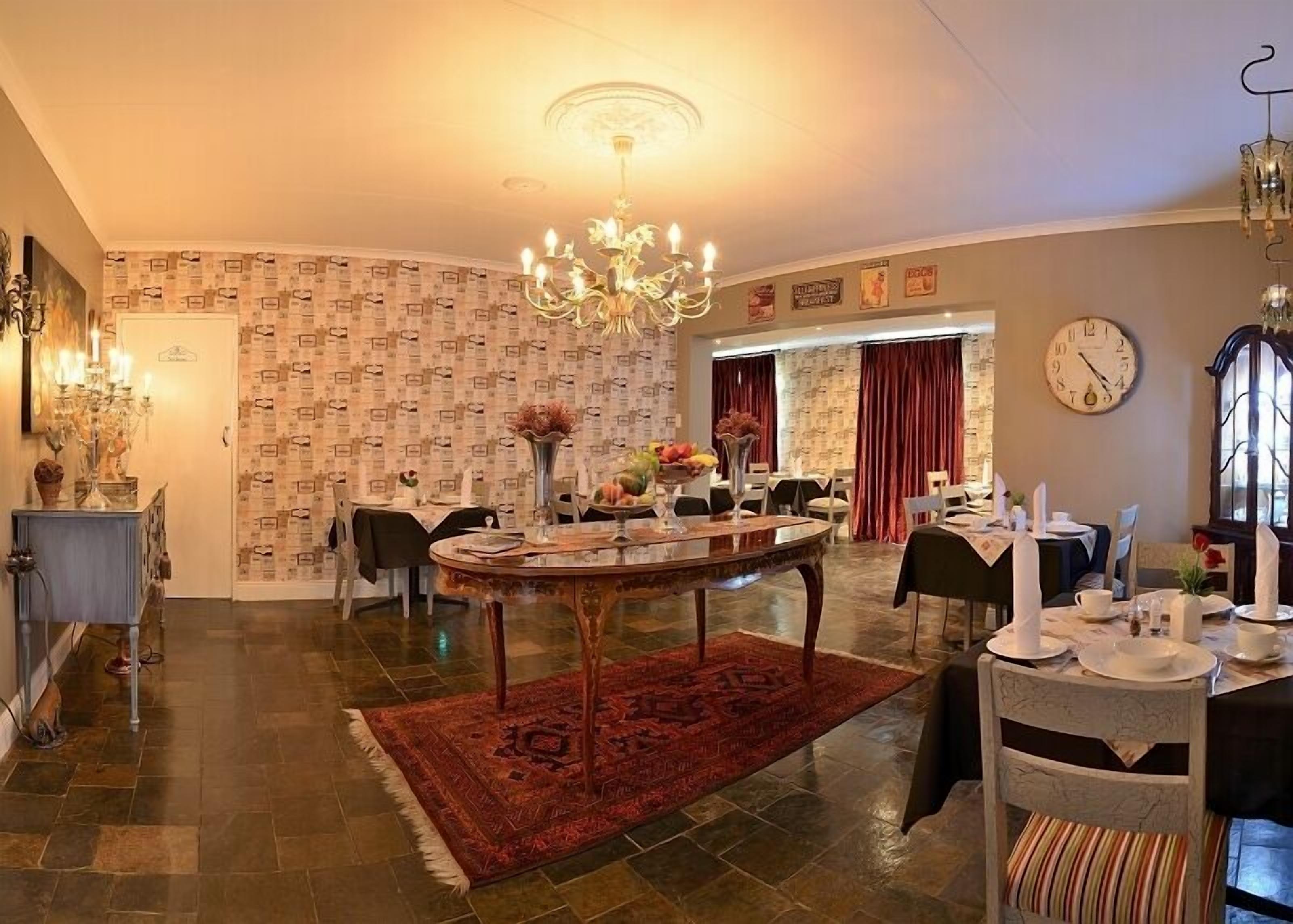 A dining area with a chandelier, patterned wallpaper, and a clock on the wall.