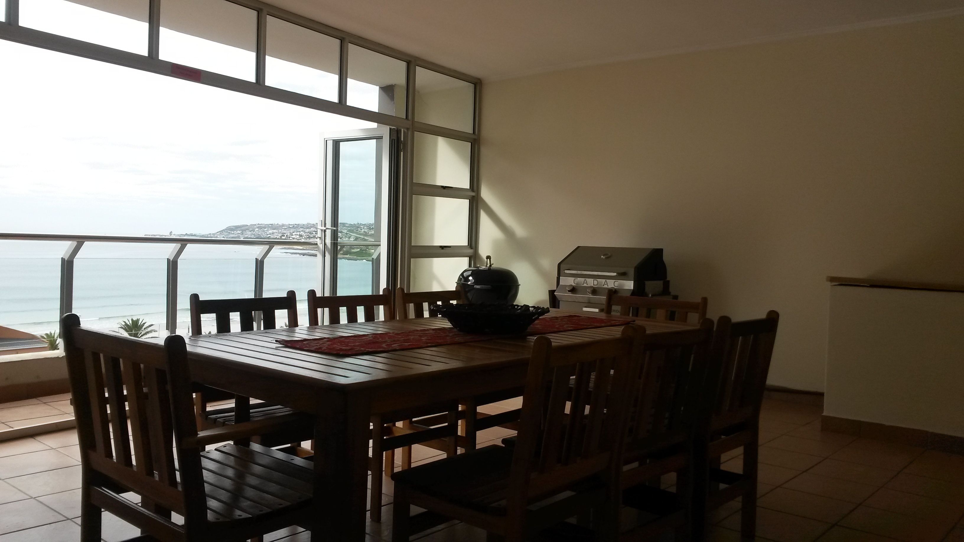 Comedor con vista al mar, una parrilla y piso de baldosas.