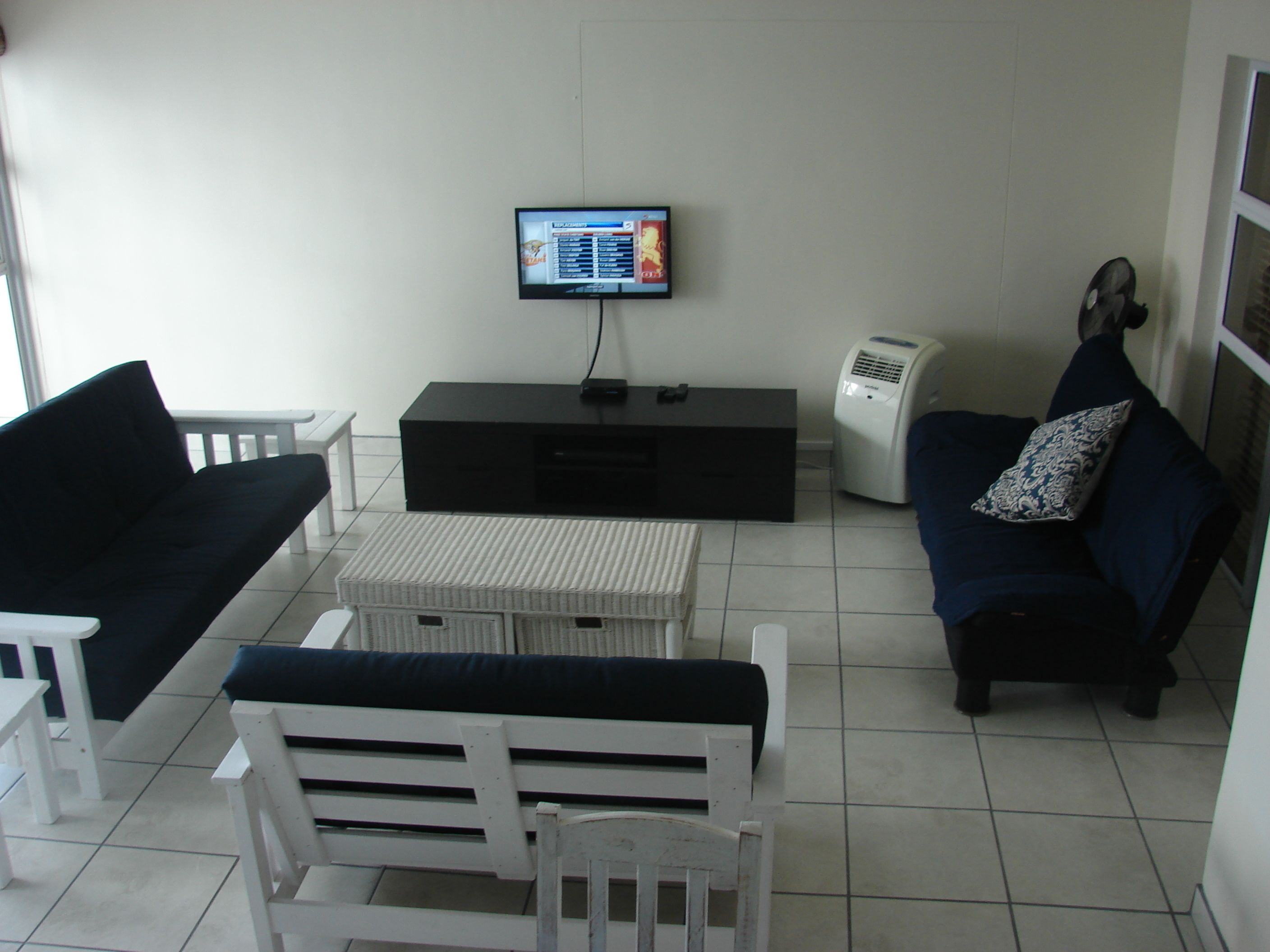A living room with a black sofa, white armchairs, a white coffee table, a black entertainment unit, and a wall-mounted TV.