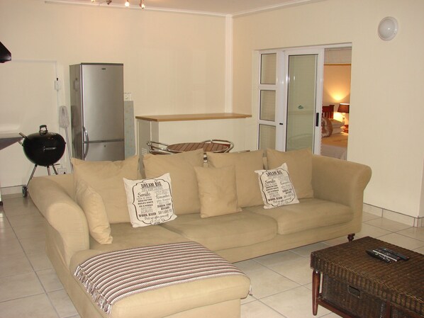 A living room with a beige sofa, a striped throw, a wicker coffee table, and a grill in the background.
