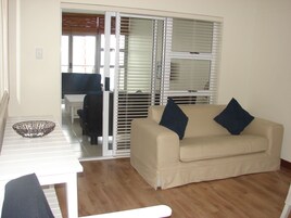 Una sala de estar con un sofá color beige, dos almohadas azul oscuro, una mesa de centro blanca y una silla negra.