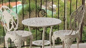 A balcony with a round table and ornate white chairs, overlooking a green landscape with buildings in the distance. - Hamelin Guest House (Bluff)
