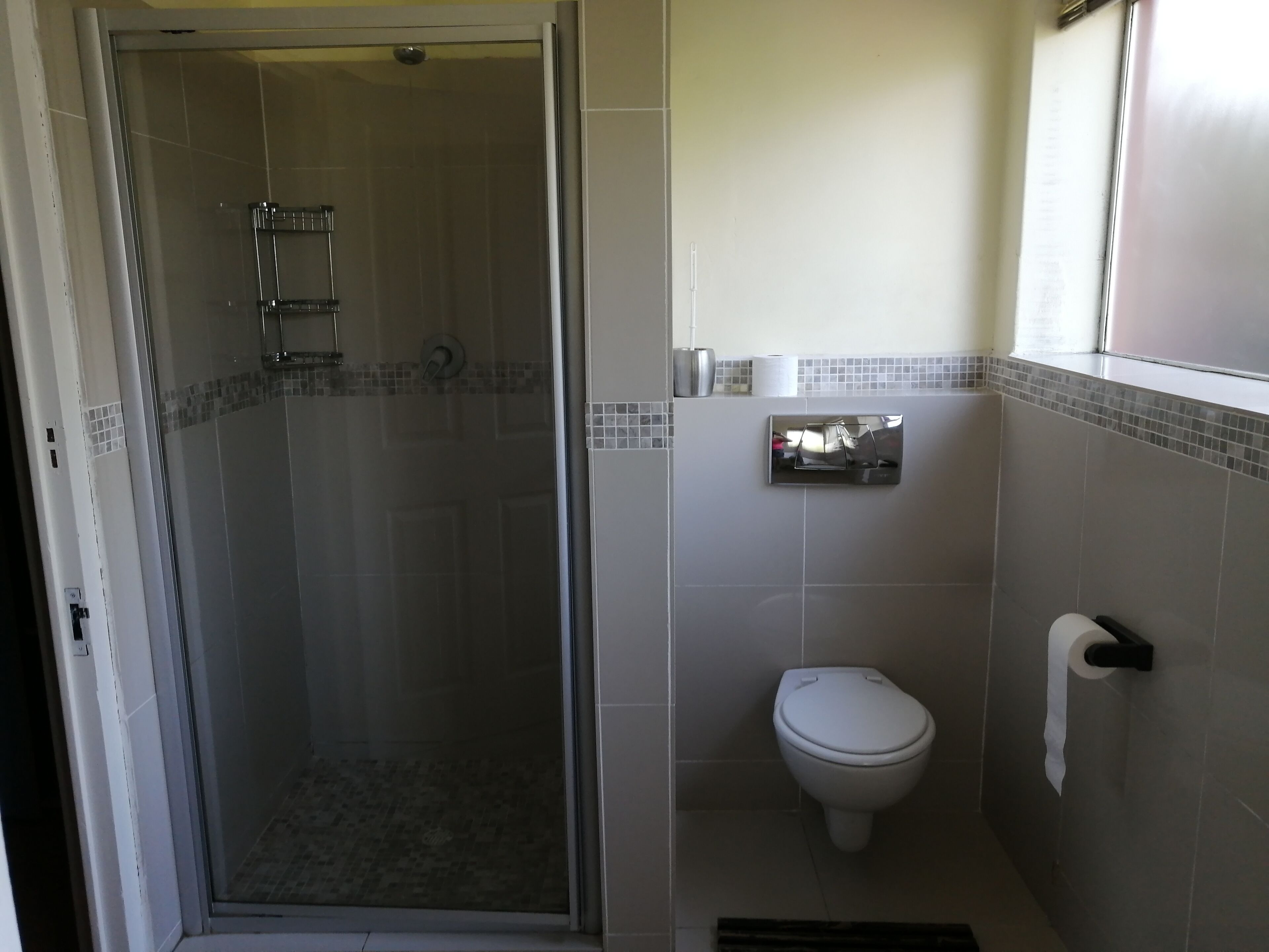 A bathroom with a glass-enclosed shower, a toilet, and a towel dispenser.