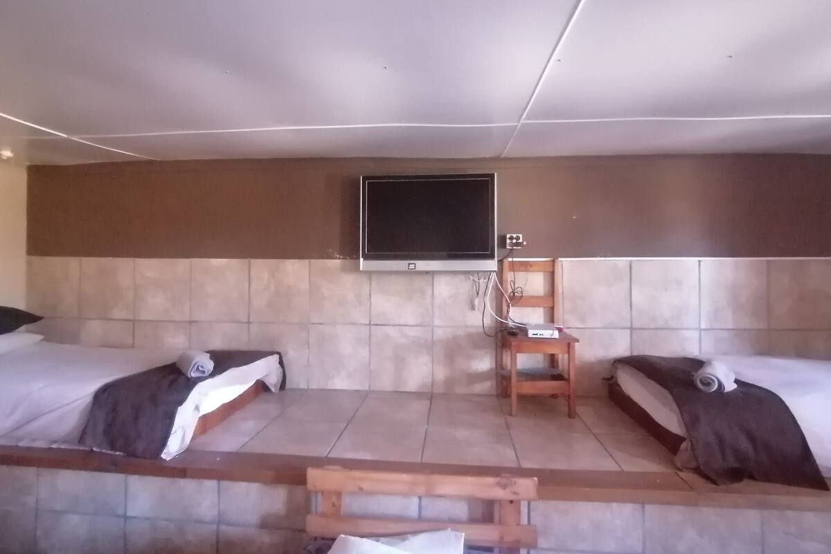 A room with two beds, a television mounted on the wall, and a wooden chair.