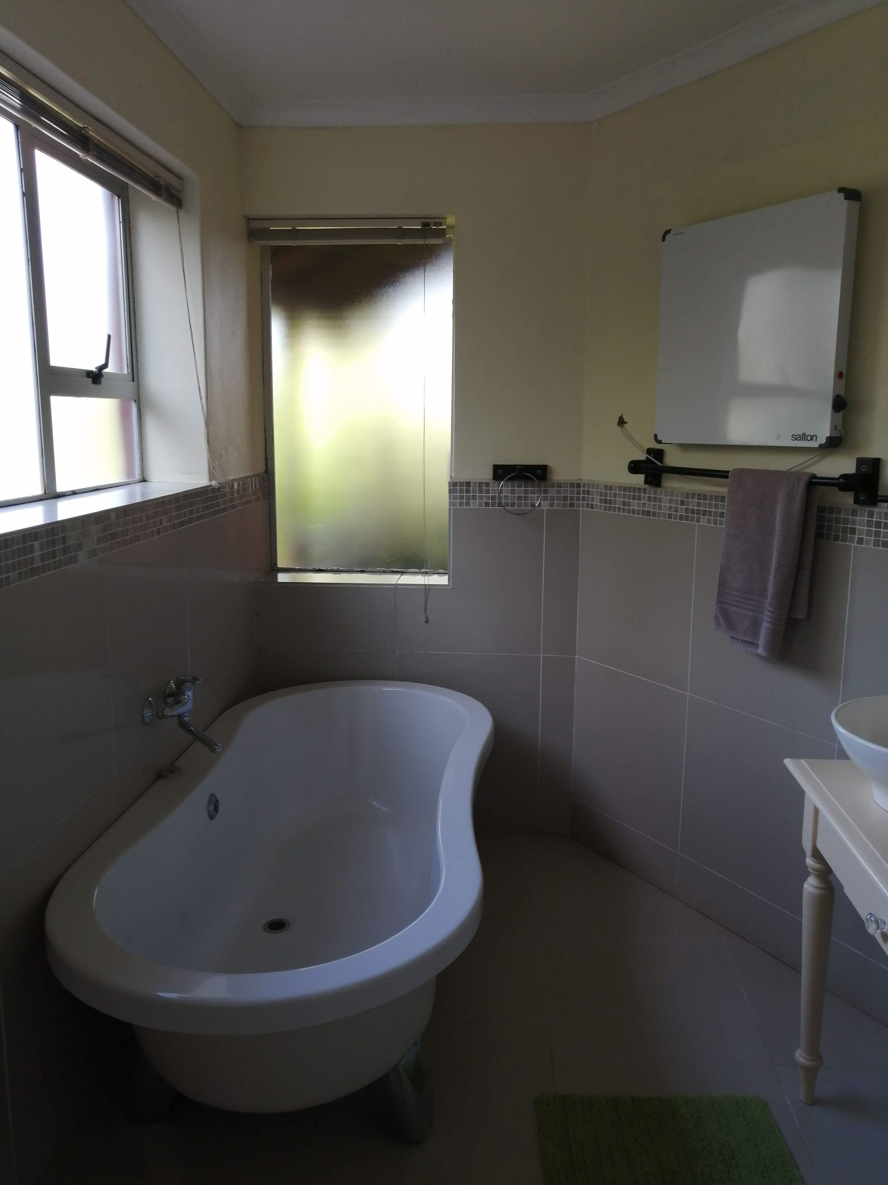 A bathroom with a freestanding bathtub, a window with blinds, a towel rack, and a white sink.