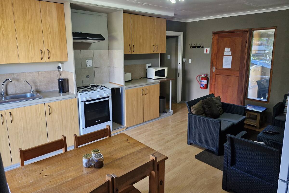A compact kitchen with wooden cabinets, a gas stove, a microwave, and a dining area with a table and chairs.