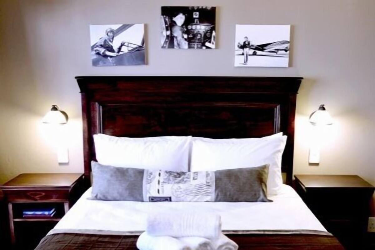 A neatly made bed with a dark headboard, white linens, and a brown bedspread. There are three wall-mounted pictures above the bed, and two bedside lamps on either side.