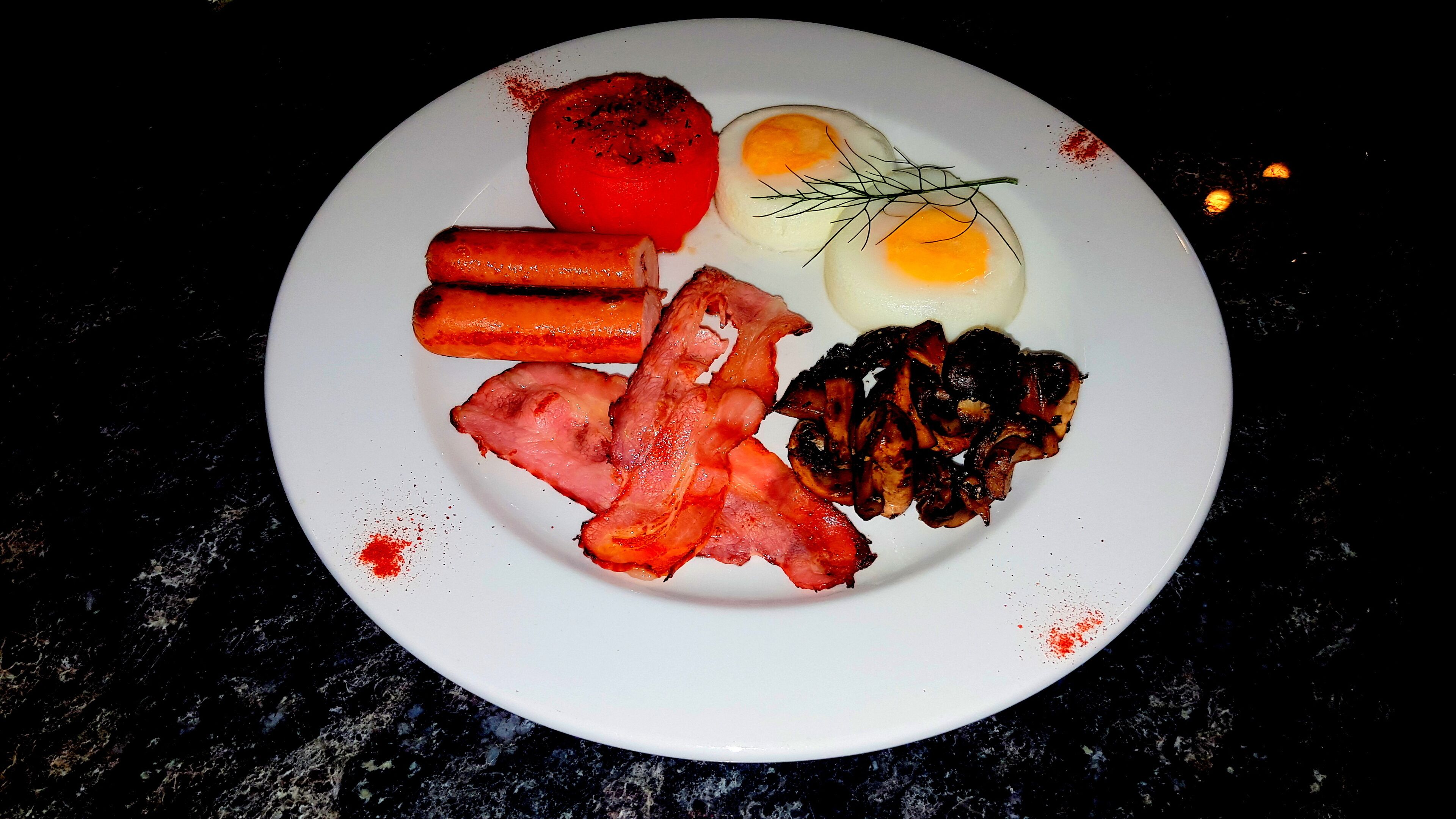 A plate of food including bacon, eggs, tomatoes, and sausages.