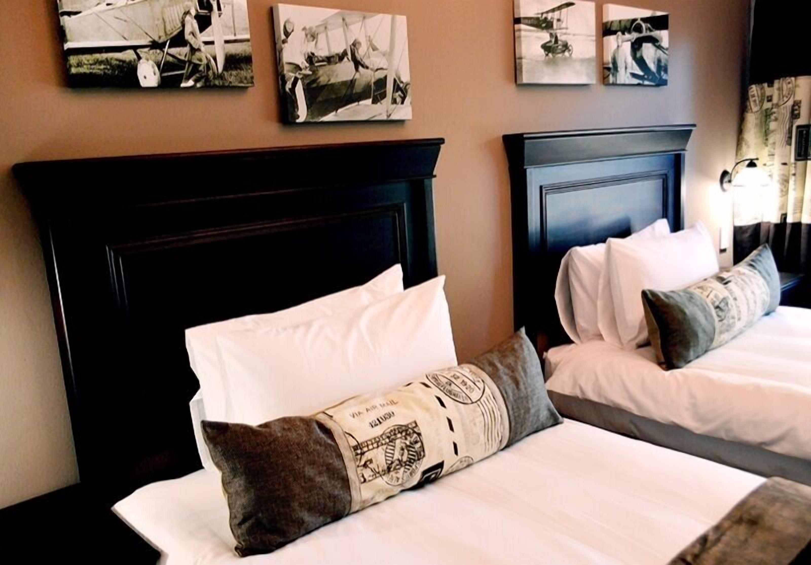 Une chambre d’hôtel avec deux lits, chacun doté de draps et d’oreillers blancs, et d’une tête de lit en bois foncé.