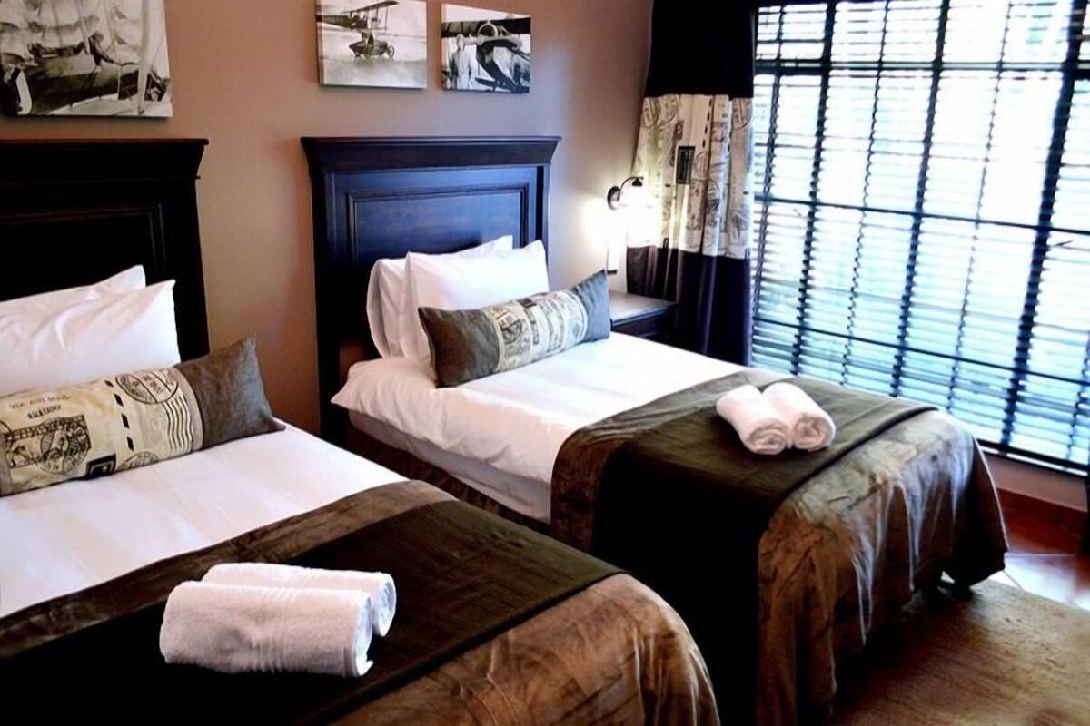 A hotel room with two beds, each with a dark headboard and white bedding. There are towels on the beds and a window with blinds.