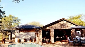 A swimming pool area with a brick building, outdoor seating, and a pergola. - Barnstormers Rest (Nkomazi)