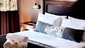 A neatly made bed with white and gray linens, a rolled towel, and a decorative pillow with a vintage design. - Barnstormers Rest (Nkomazi)