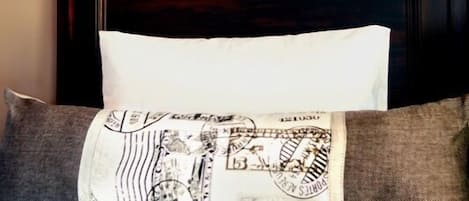 Una cama con cabecera de madera oscura, almohada blanca y almohada estampada. Dos cuadros de aviones en blanco y negro adornan la pared sobre la cama.