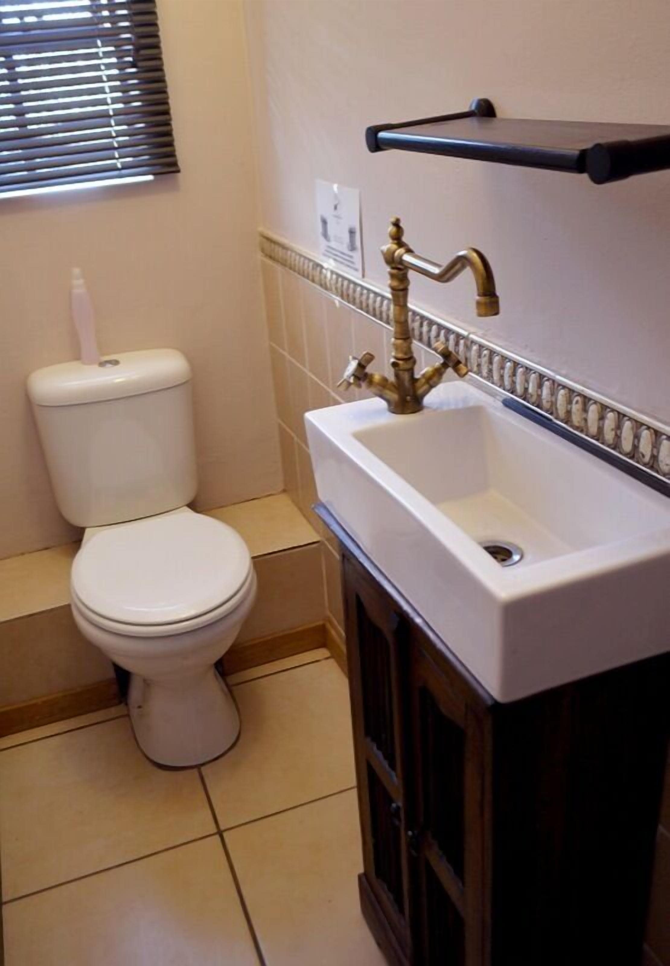 A bathroom with a toilet, a sink with a brass faucet, and a towel rack above the sink.