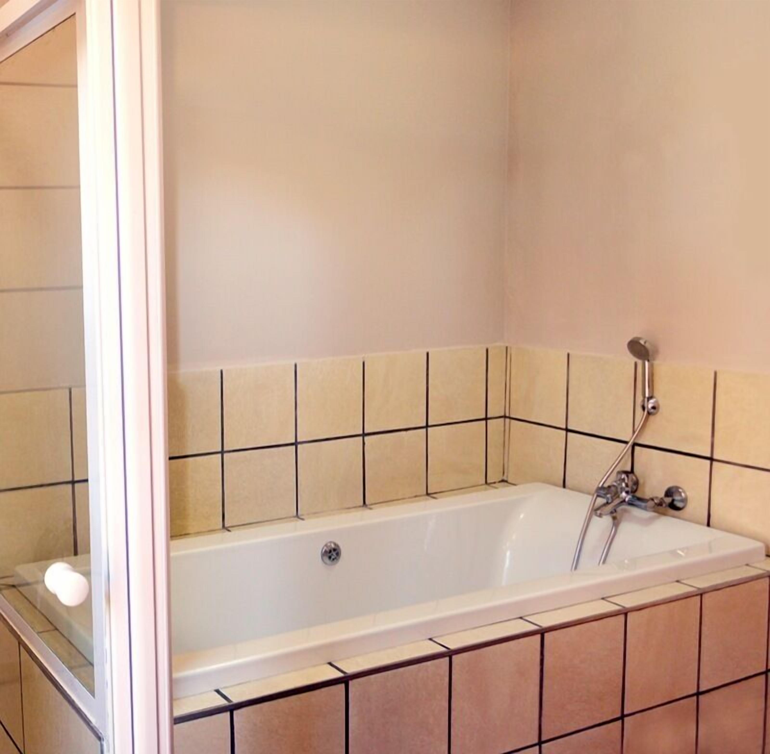 Un baño con una bañera blanca, paredes enlosadas y zona de ducha.