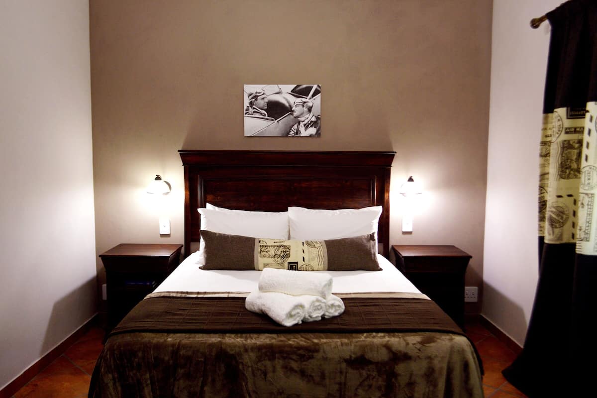 A neatly made bed with a brown bedspread, two pillows, and a folded towel. There is a framed picture above the bed and two bedside lamps on either side.