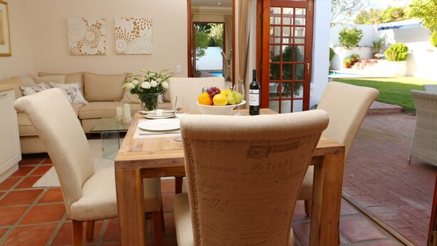 A dining area with a wooden table, beige chairs, and a bowl of fruit. - Constantia Garden Suites (Cape Town)