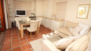 A living room with a sofa, a coffee table, a TV, and a dining area with chairs and a table. - Constantia Garden Suites (Cape Town)