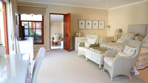 A spacious bedroom with a large bed, a sitting area with a chair and table, and a view through an open door to a balcony. - Constantia Garden Suites (Cape Town)