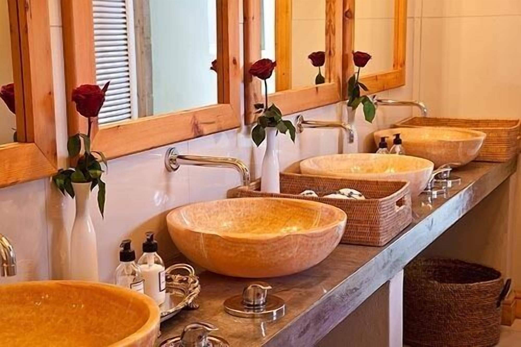 Ein Badezimmer mit drei großen, ovalen Waschbecken aus Holz, einem Spiegel mit Rosenornamenten und einem Metallarmaturen.