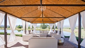 Un espace extérieur aménagé, abrité et doté de mobilier en osier, offrant une vue sur un lac et des montagnes.
