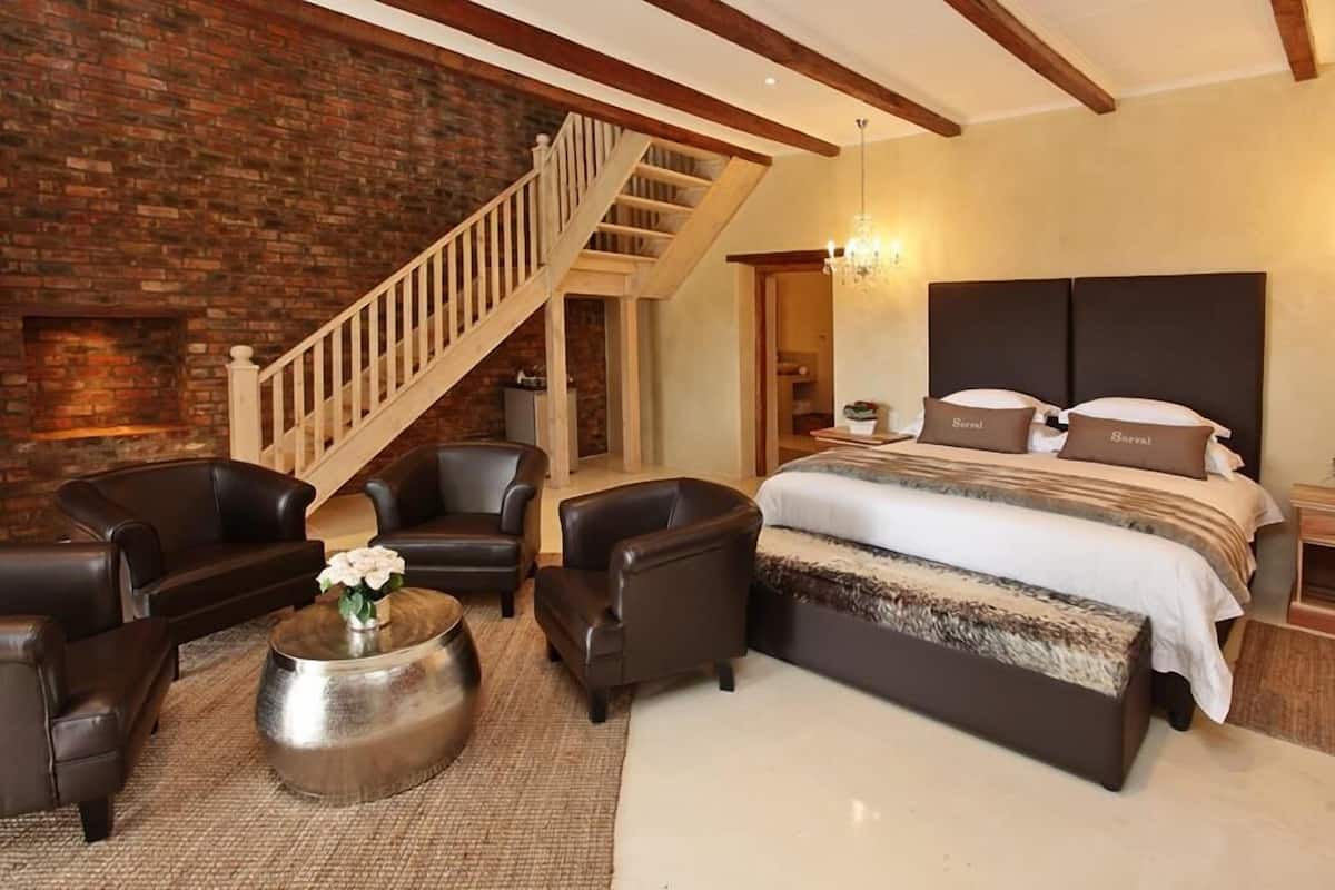 Une chambre à coucher avec un grand lit, un escalier en bois, des fauteuils en cuir et une table basse.