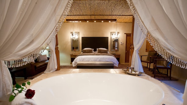 Une chambre à coucher luxueuse avec une grande baignoire, un lit avec deux oreillers et un miroir au mur.