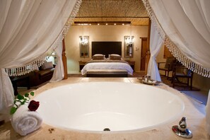 Une chambre à coucher luxueuse avec une grande baignoire, un lit avec deux oreillers et un miroir au mur.