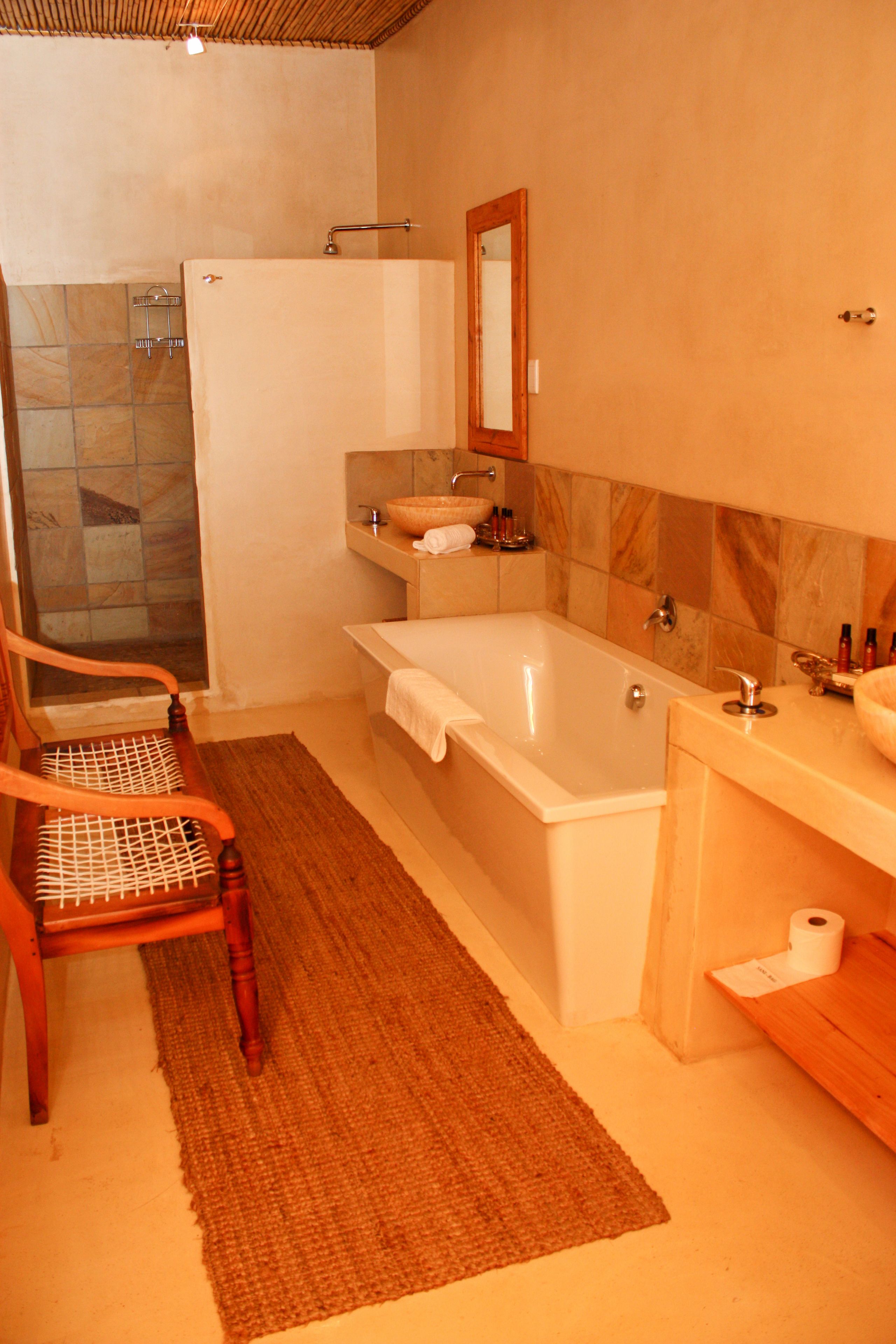A bathroom with a bathtub, a wooden chair, a towel rack, and a mirror.