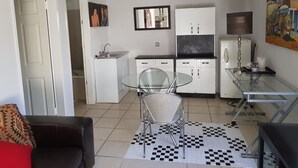 A compact living space with a kitchenette, a dining area with a glass table and metal chairs, and a sofa with a patterned cushion. - Mi Casa Su Casa Boutique Accommodation (Johannesburg)