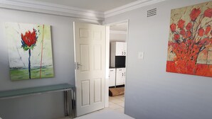 A room with a bed, a desk with a glass top, and two paintings on the walls. - Mi Casa Su Casa Boutique Accommodation (Johannesburg)