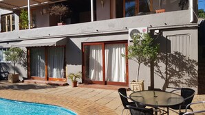 A poolside area with a glass table and chairs, a covered patio, and a building with multiple windows and doors. - Mi Casa Su Casa Boutique Accommodation (Johannesburg)