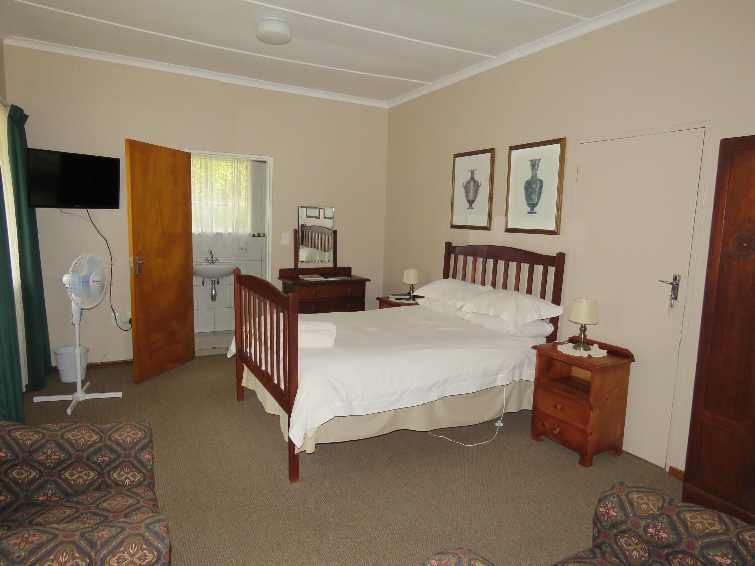 A bedroom with a bed, bedside tables, a mirror, a fan, a dresser, and two framed pictures on the wall.