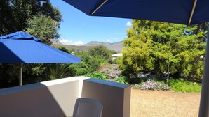 Un balcon avec une table et des chaises, un parasol bleu et une vue sur la verdure et les montagnes.