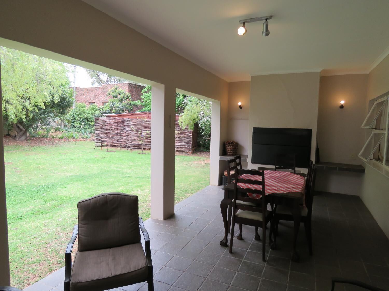A covered patio area with a dining table, chairs, and a flat-screen TV.