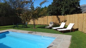 Un jardin avec une piscine, une clôture en bois et deux chaises longues.