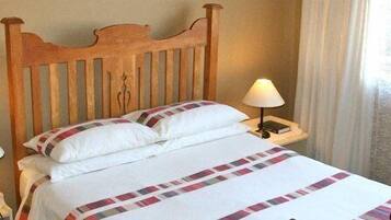 Una cama bien hecha con cabecera de madera, dos lámparas de noche y una ventana con cortinas.