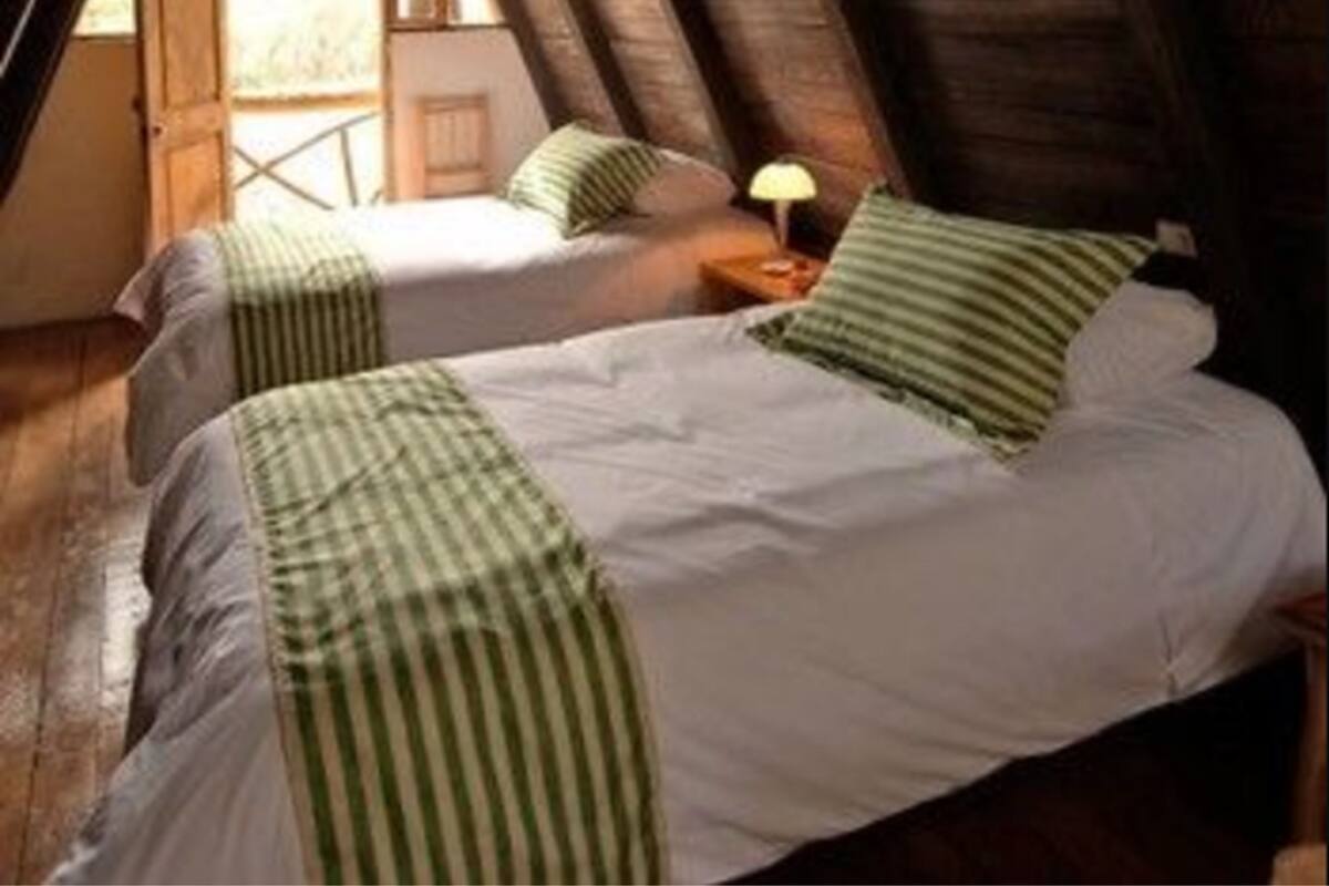 Une chambre confortable située sous les toits, avec deux lits, des poutres en bois et une petite table avec une lampe.