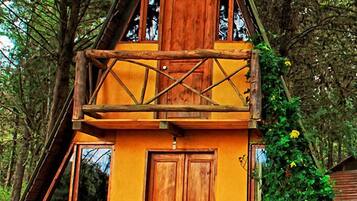 Una cabaña de madera de dos pisos con balcón, rodeada de árboles.