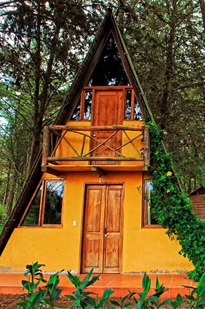 A two-story wooden cabin with a balcony, surrounded by trees.