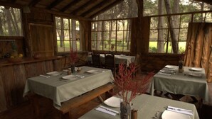 A rustic dining area with wooden tables and benches, large windows, and a natural view. - Inraki Lodge (Guayllabamba)