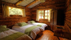 A log cabin room with two beds, wooden floors, and a wardrobe. - Inraki Lodge (Guayllabamba)