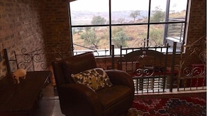 A cozy room with a large window, a brown leather sofa with a patterned pillow, and a red patterned rug. - The Warehouse (Krugersdorp)